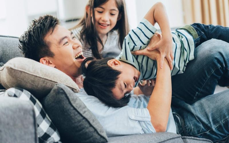 father plays on a couch with his young children